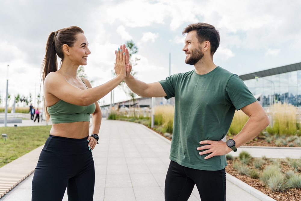 Smiling, athletic couple jogging in a sunny, forested area, enjoying an energetic workout in nature - Butler Spine & Sport