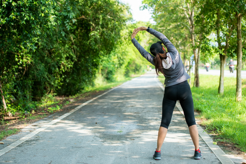 Smiling, athletic couple jogging in a sunny, forested area, enjoying an energetic workout in nature - Butler Spine & Sport Asian runner people workout fitness session - Back Pain in Overland Park