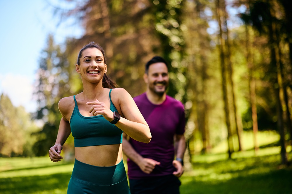 Smiling, athletic couple jogging in a sunny, forested area, enjoying an energetic workout in nature - Butler Spine & Sport