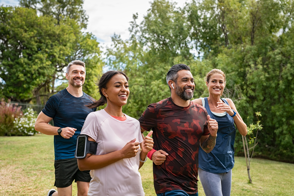 Smiling, athletic couple jogging in a sunny, forested area, enjoying an energetic workout in nature - Butler Spine & Sport