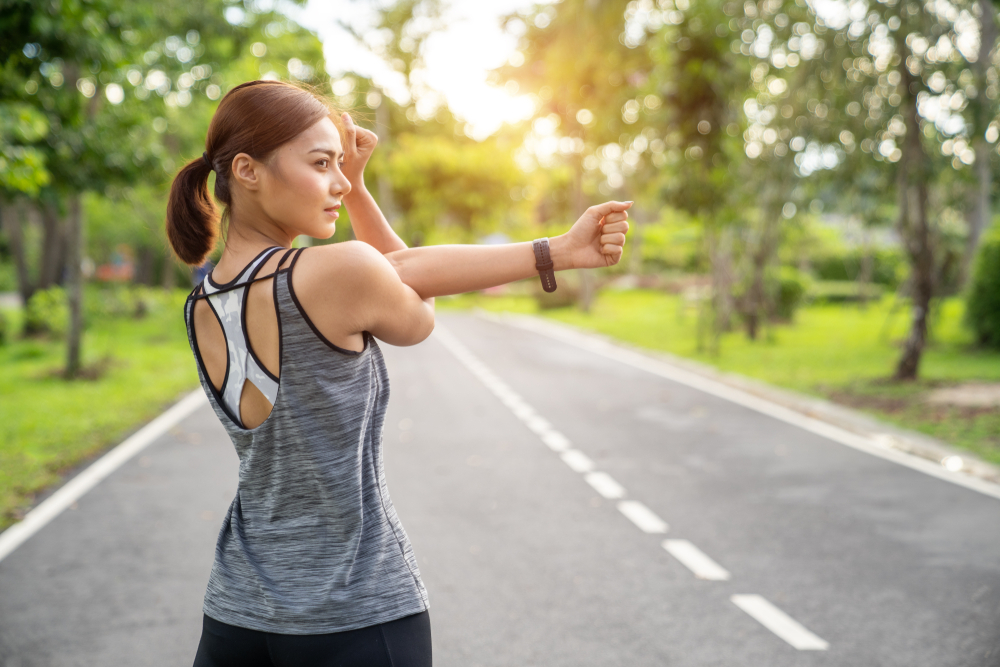 Smiling, athletic couple jogging in a sunny, forested area, enjoying an energetic workout in nature - Butler Spine & Sport Women stretching for warming up before running or working out - Cupping Therapy in Overland Park