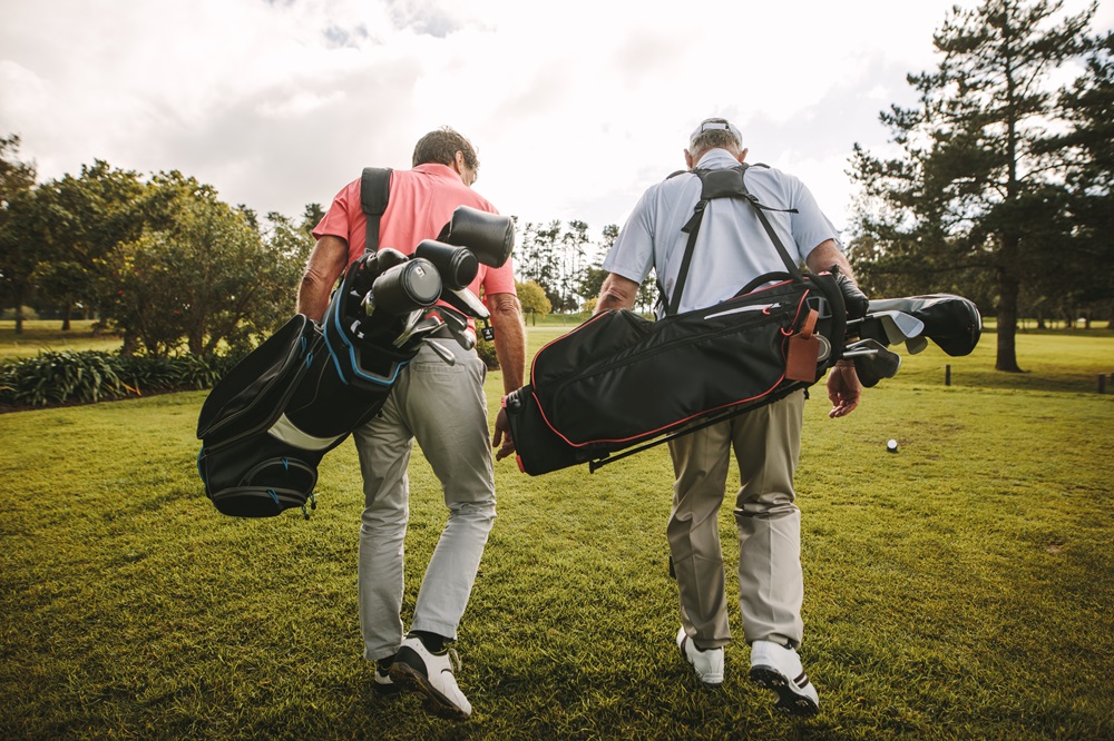 Two golfers walking together on a golf course, carrying their bags as they head towards the next hole, conveying camaraderie and a peaceful outdoor setting - Butler Spine & Sport